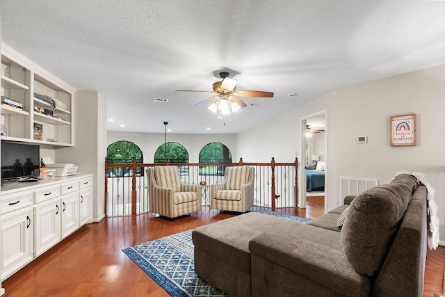 living area with a ceiling fan, visible vents, baseboards, and wood finished floors