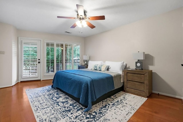 bedroom with ceiling fan, wood finished floors, visible vents, baseboards, and access to exterior