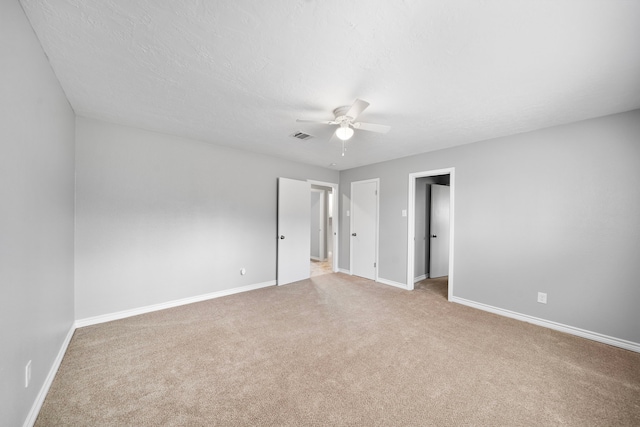 unfurnished room with light carpet, a textured ceiling, a ceiling fan, and baseboards