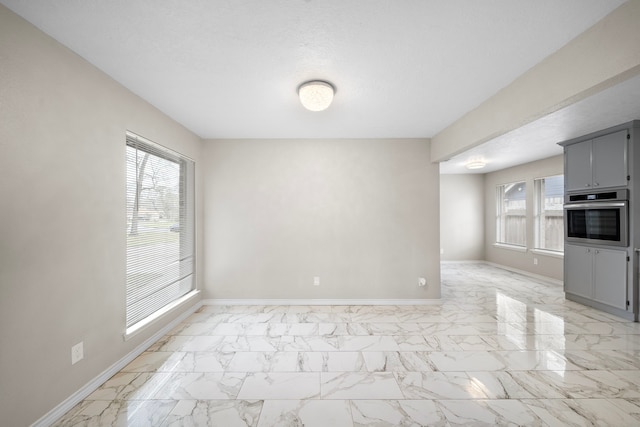 empty room featuring marble finish floor, plenty of natural light, and baseboards