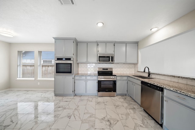 kitchen featuring decorative backsplash, marble finish floor, stainless steel appliances, gray cabinetry, and a sink