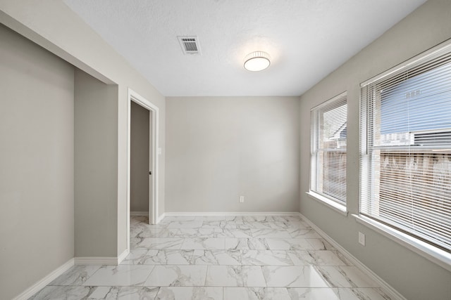 spare room with marble finish floor, visible vents, a textured ceiling, and baseboards