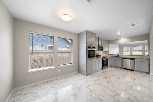 kitchen with gray cabinetry, stainless steel appliances, visible vents, baseboards, and decorative backsplash