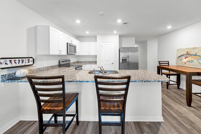 kitchen with dark wood-style floors, stainless steel appliances, visible vents, a sink, and a peninsula