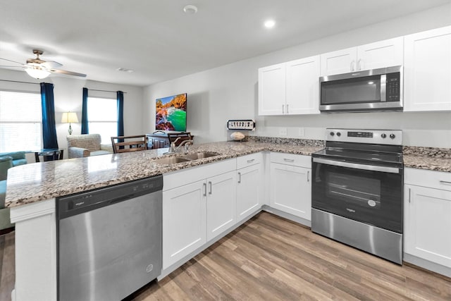 kitchen featuring stainless steel appliances, a peninsula, a sink, open floor plan, and light wood-type flooring