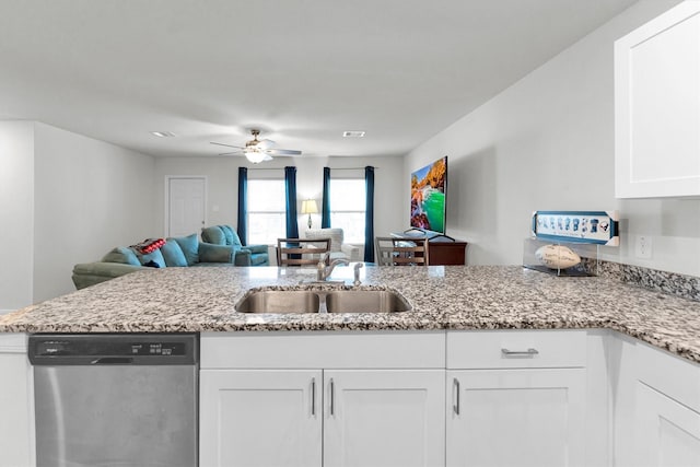 kitchen featuring light stone counters, open floor plan, stainless steel dishwasher, white cabinetry, and a sink