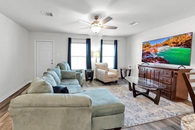 living room with a ceiling fan, visible vents, baseboards, and wood finished floors