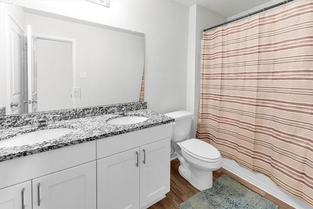 bathroom featuring double vanity, a sink, toilet, and wood finished floors