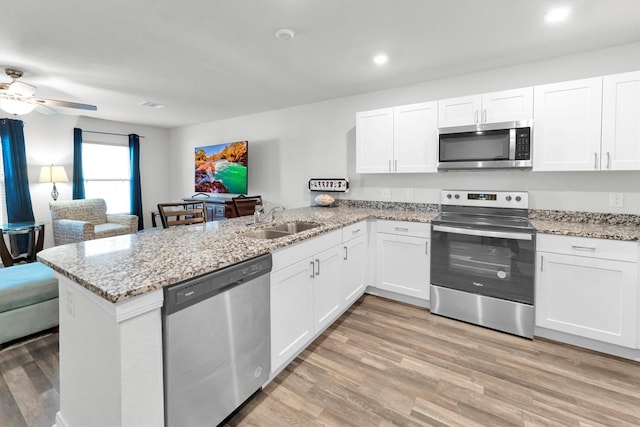 kitchen featuring a peninsula, stainless steel appliances, light wood-style floors, white cabinetry, and a sink