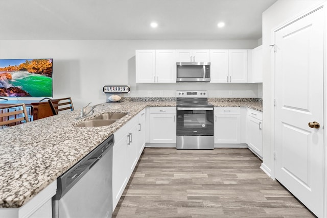 kitchen with light wood-style flooring, stainless steel appliances, a peninsula, a sink, and white cabinets