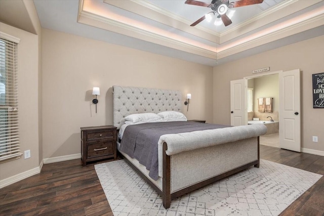 bedroom featuring a tray ceiling, crown molding, baseboards, ensuite bathroom, and wood finished floors
