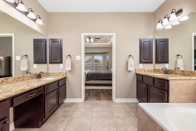 ensuite bathroom featuring a sink, two vanities, and baseboards