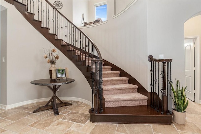 stairway with stone tile flooring, arched walkways, baseboards, and a towering ceiling