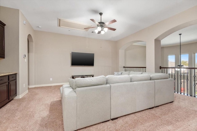 living area featuring attic access, light colored carpet, baseboards, arched walkways, and ceiling fan