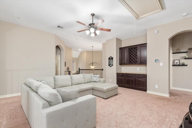 living area with baseboards, ceiling fan, attic access, arched walkways, and light colored carpet