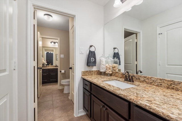 bathroom featuring baseboards, toilet, tile patterned floors, two vanities, and a sink