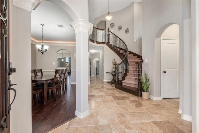 foyer entrance featuring stairs, stone finish floor, a towering ceiling, arched walkways, and visible vents