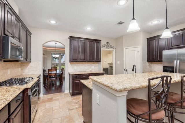kitchen featuring a kitchen bar, washing machine and dryer, visible vents, stone tile flooring, and appliances with stainless steel finishes