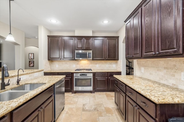 kitchen featuring decorative light fixtures, decorative backsplash, a sink, arched walkways, and appliances with stainless steel finishes