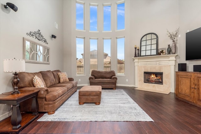 living area with a towering ceiling, baseboards, a fireplace, and dark wood finished floors
