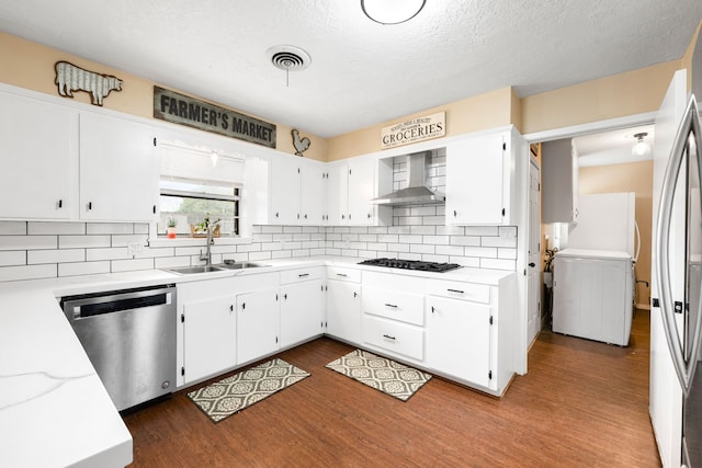 kitchen featuring visible vents, appliances with stainless steel finishes, dark wood-type flooring, a sink, and wall chimney exhaust hood