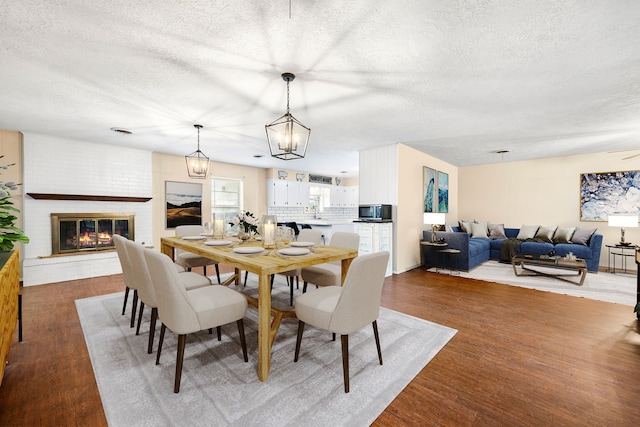 dining room featuring a brick fireplace, a textured ceiling, and wood finished floors