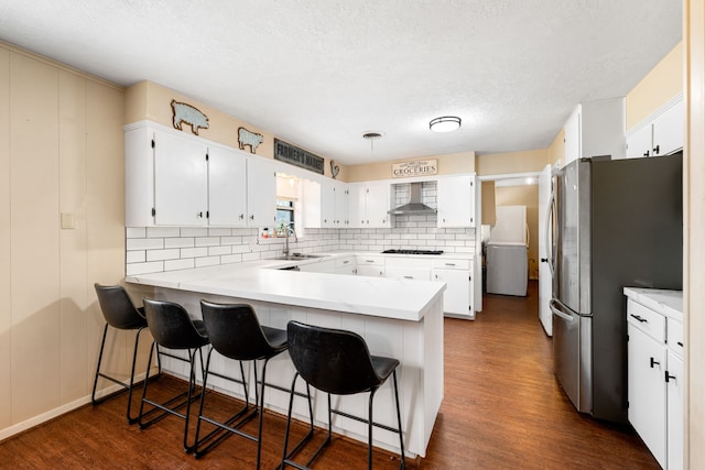 kitchen featuring refrigerator, gas stovetop, freestanding refrigerator, wall chimney range hood, and a peninsula