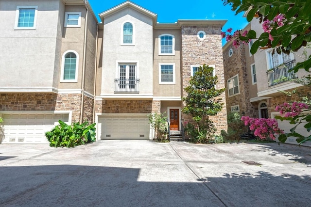 multi unit property featuring a garage, driveway, stone siding, and stucco siding