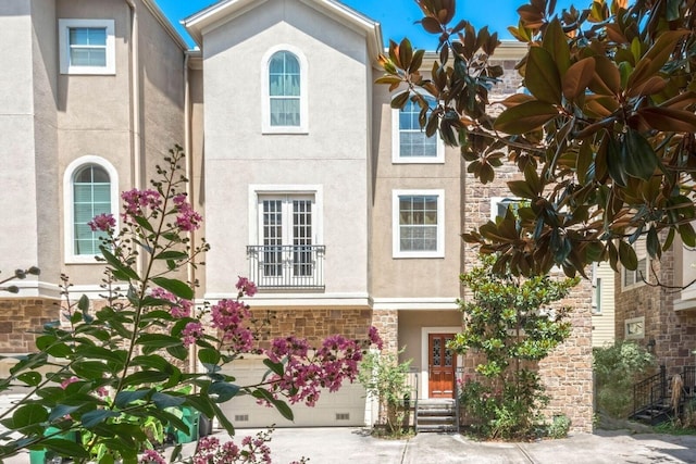 view of property featuring an attached garage, stone siding, concrete driveway, and stucco siding