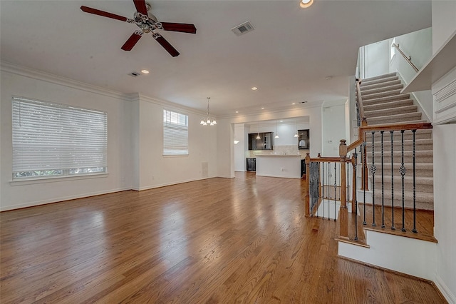 unfurnished living room with stairs, ornamental molding, wood finished floors, and visible vents