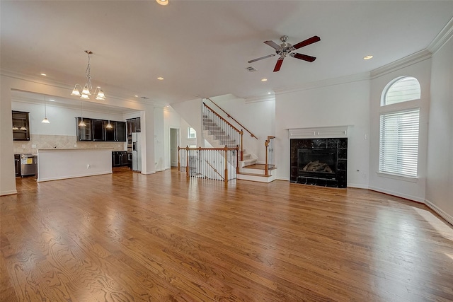 unfurnished living room with stairway, ornamental molding, a tiled fireplace, and wood finished floors