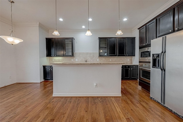 kitchen with appliances with stainless steel finishes, light wood-type flooring, ornamental molding, and a kitchen island