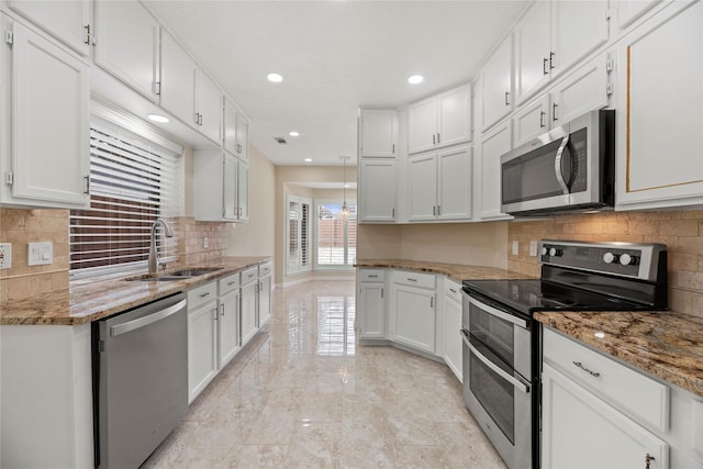 kitchen featuring light stone counters, marble finish floor, appliances with stainless steel finishes, white cabinetry, and a sink