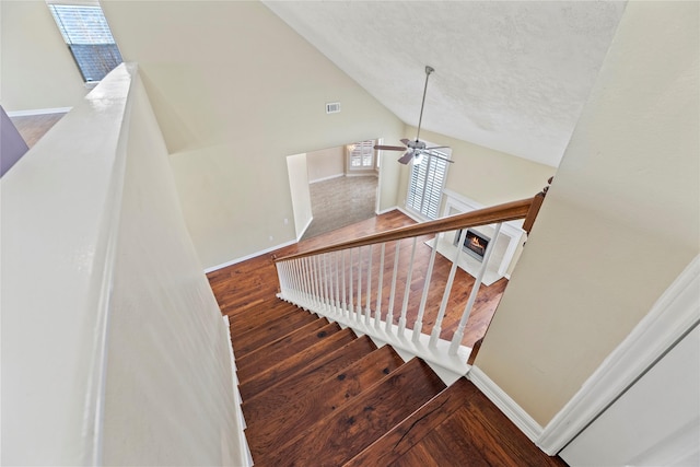 stairs with baseboards, visible vents, a ceiling fan, wood finished floors, and high vaulted ceiling