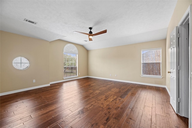 empty room featuring dark wood-style flooring, visible vents, baseboards, vaulted ceiling, and a ceiling fan