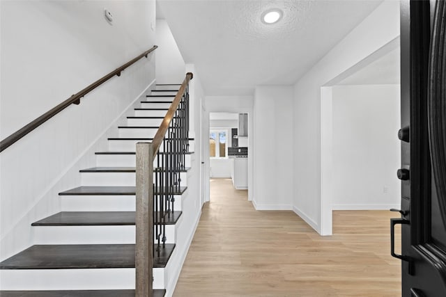 foyer featuring a textured ceiling, stairway, baseboards, and light wood-style floors