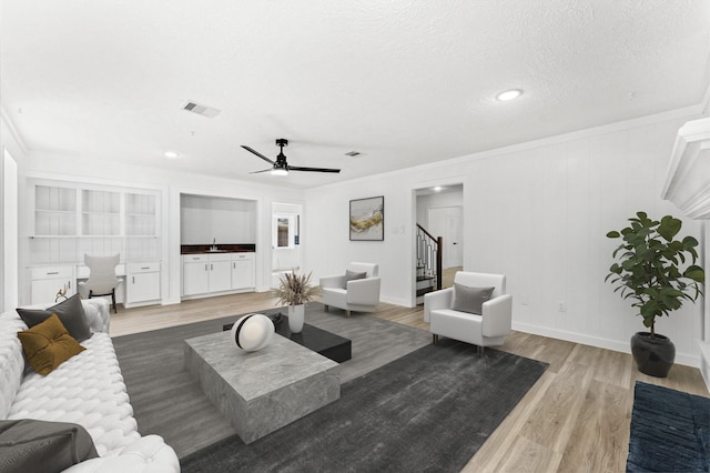 living area featuring visible vents, ornamental molding, stairs, a textured ceiling, and light wood-type flooring