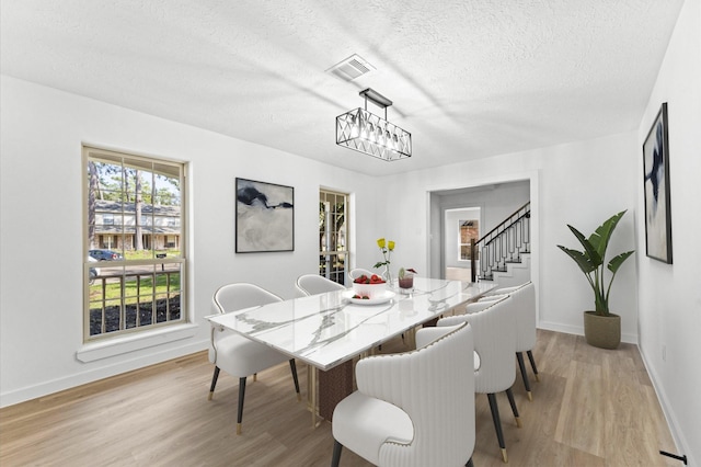 dining area with a textured ceiling, baseboards, visible vents, and light wood-style floors