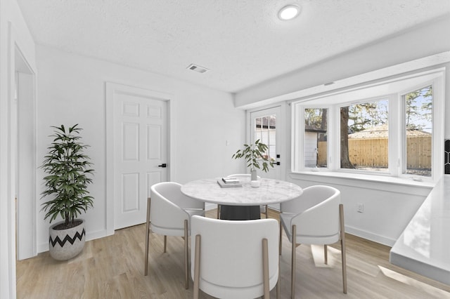 dining room featuring a textured ceiling, light wood-style flooring, visible vents, and baseboards