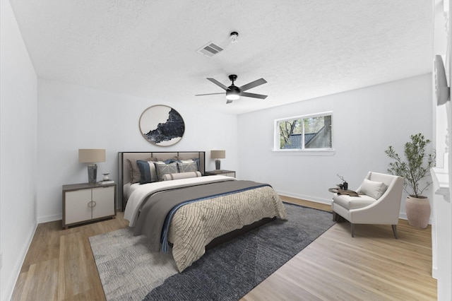 bedroom with visible vents, light wood-style flooring, ceiling fan, a textured ceiling, and baseboards