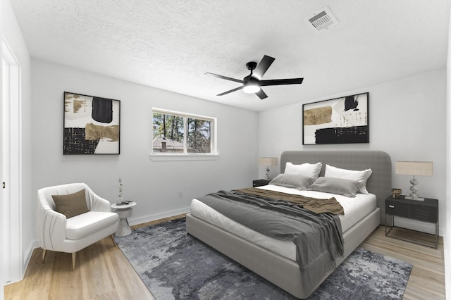 bedroom featuring a textured ceiling, ceiling fan, wood finished floors, visible vents, and baseboards