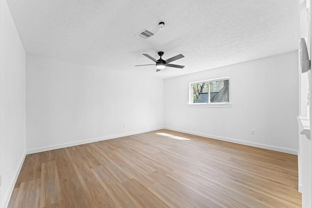 spare room featuring baseboards, visible vents, a ceiling fan, a textured ceiling, and light wood-type flooring