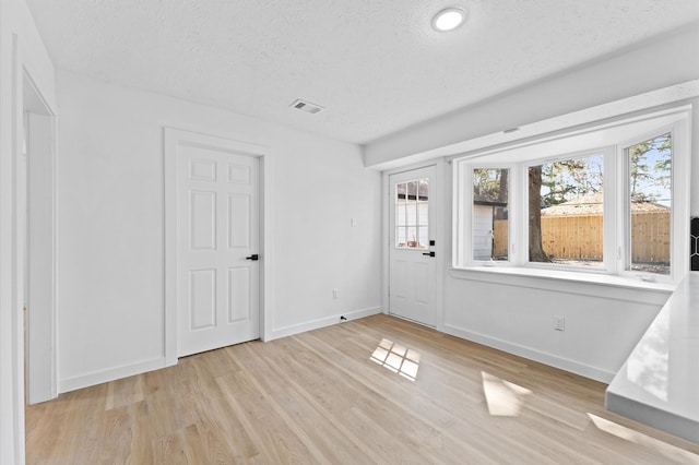 interior space featuring a textured ceiling, light wood-style flooring, visible vents, and baseboards