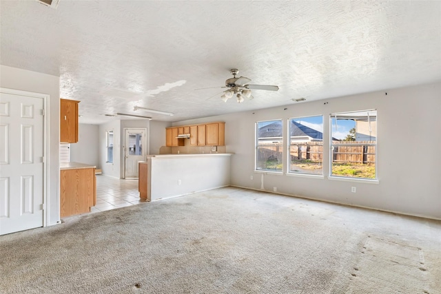 unfurnished living room with a textured ceiling, light tile patterned floors, light colored carpet, a ceiling fan, and visible vents