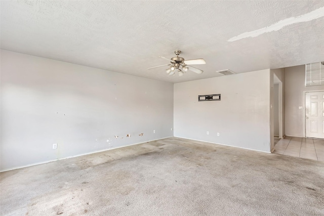 spare room featuring a ceiling fan, light colored carpet, visible vents, and a textured ceiling