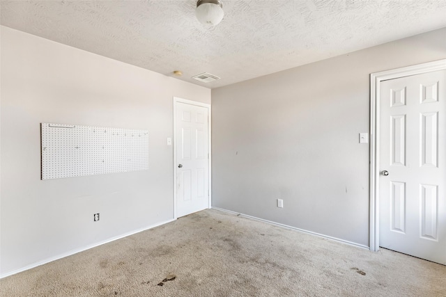 empty room with carpet floors, visible vents, a textured ceiling, and baseboards