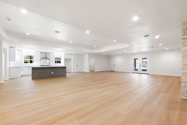 unfurnished living room with a tray ceiling, a textured ceiling, french doors, light wood-type flooring, and recessed lighting