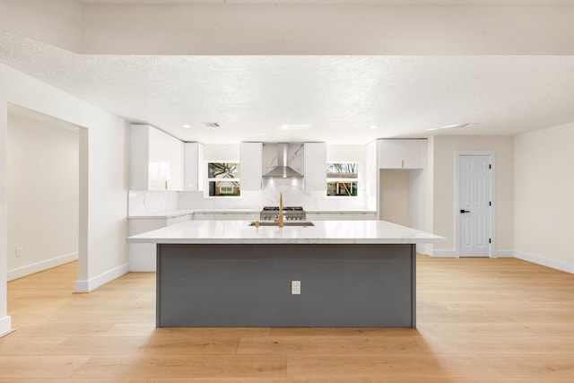 kitchen with light wood finished floors, wall chimney exhaust hood, white cabinetry, and a sink