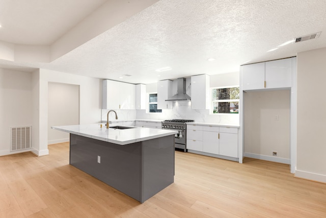 kitchen featuring wall chimney range hood, visible vents, stainless steel range, and a sink