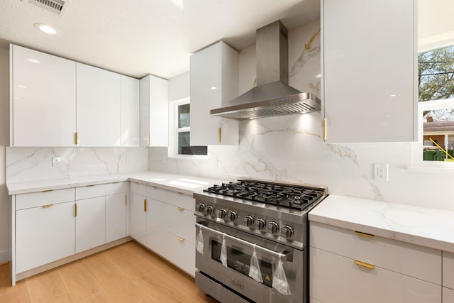 kitchen with wall chimney exhaust hood, high end stainless steel range, visible vents, and white cabinets